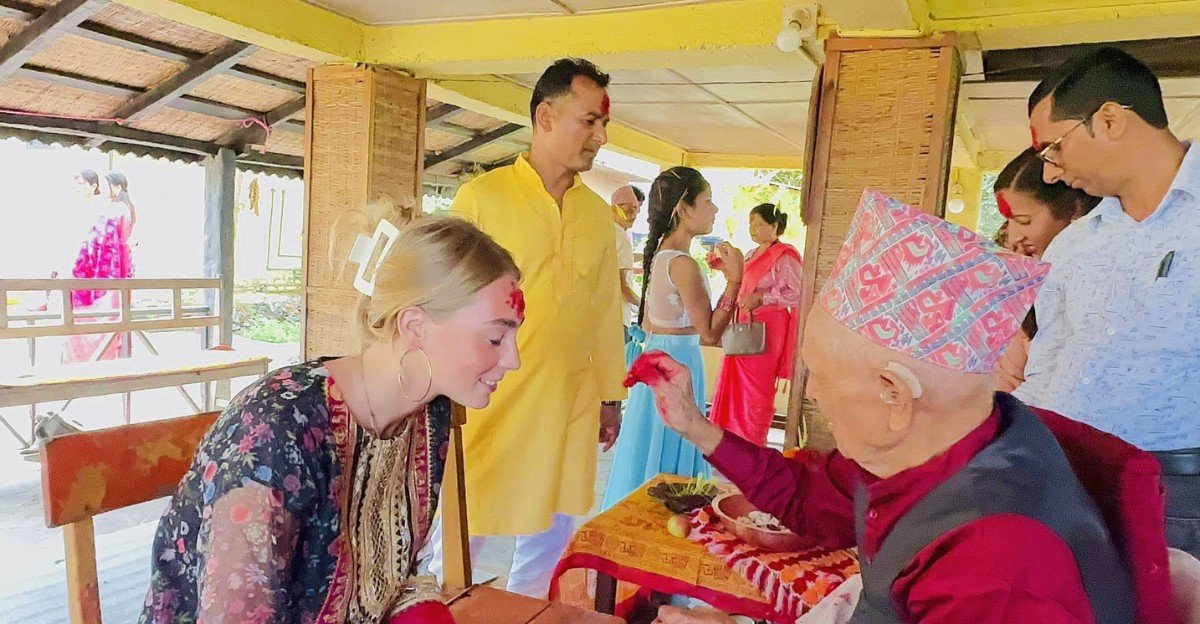 A foreign tourist receiving red tika and jamara from a local Nepali family during Dashain celebrations
